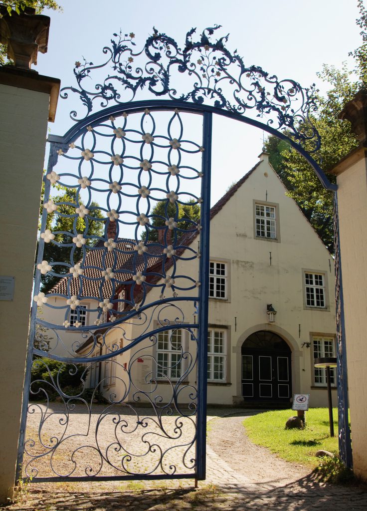 Blick durch das mit Blumen verzierte Franzosentor auf das ehemalige Gutshaus Haus Riensberg.