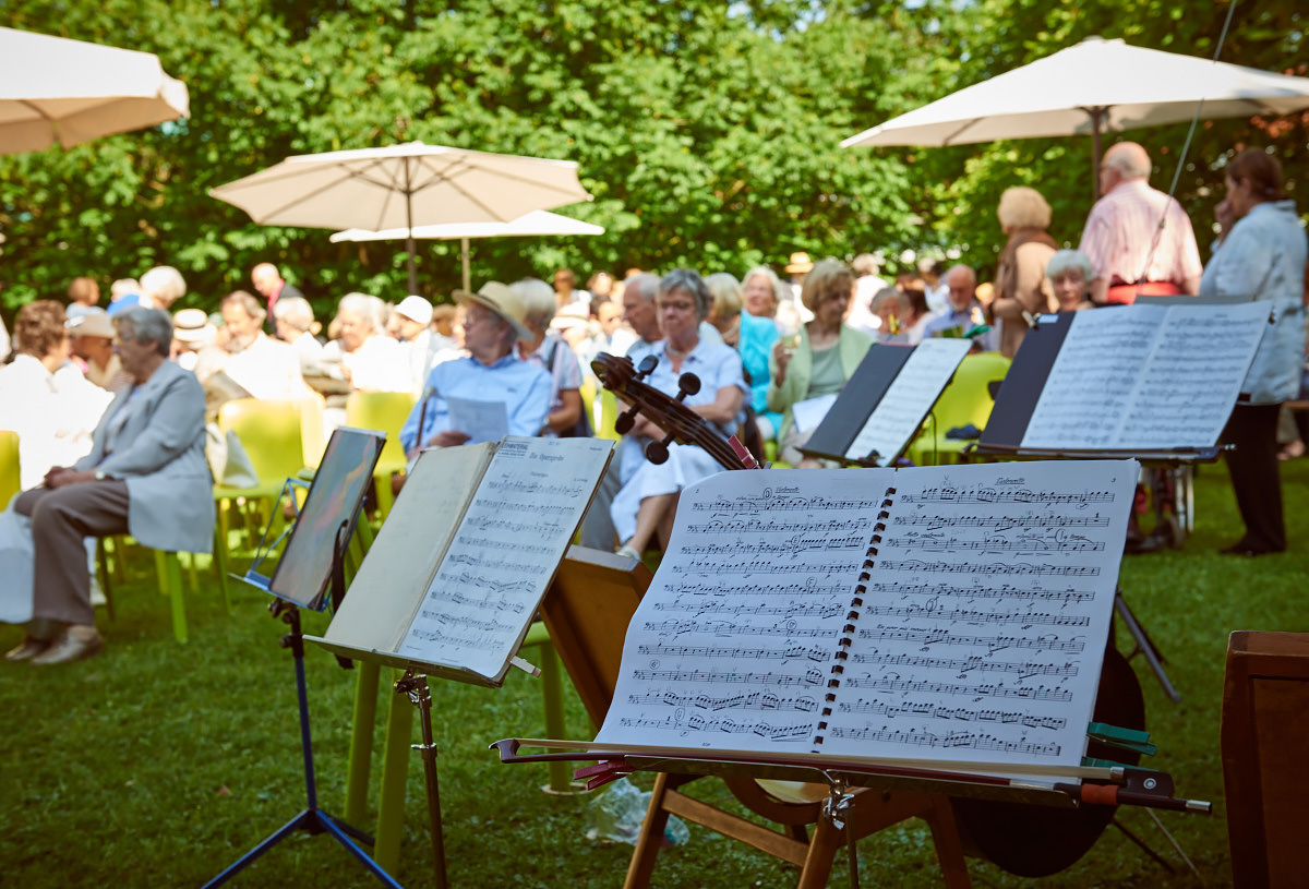 Konzertpublikum im Park. Im Vordergrund ein Notenständer