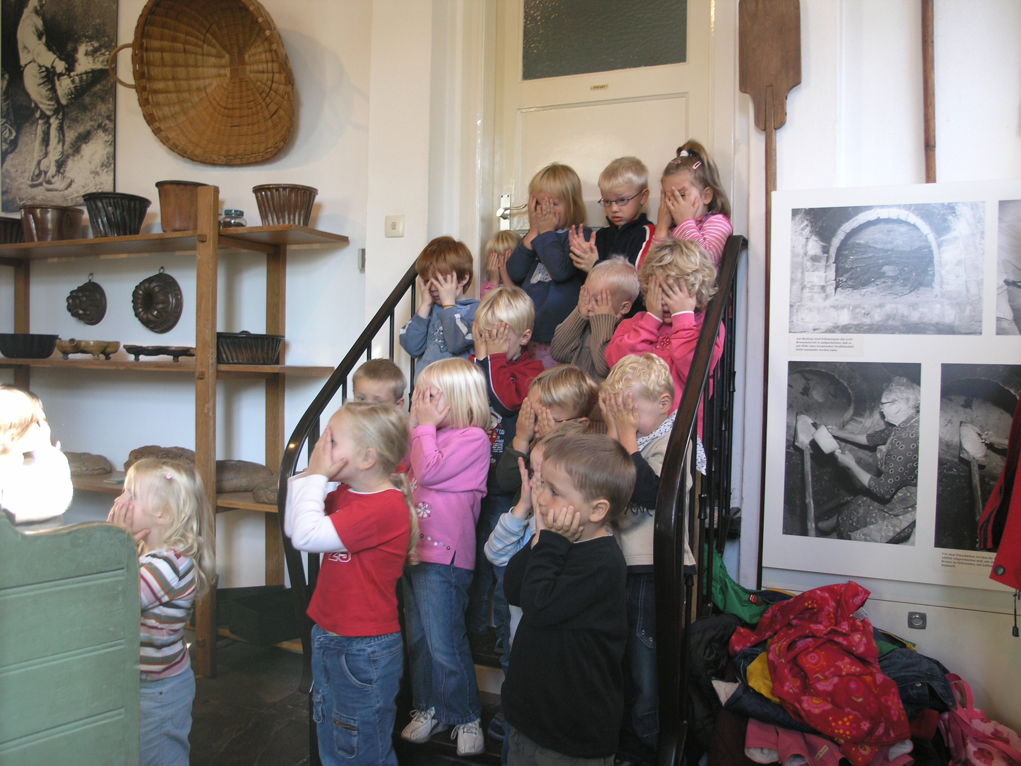Kindergartengruppe auf einer Treppe in der Mühle. Sie halten sich alle die Augen zu.