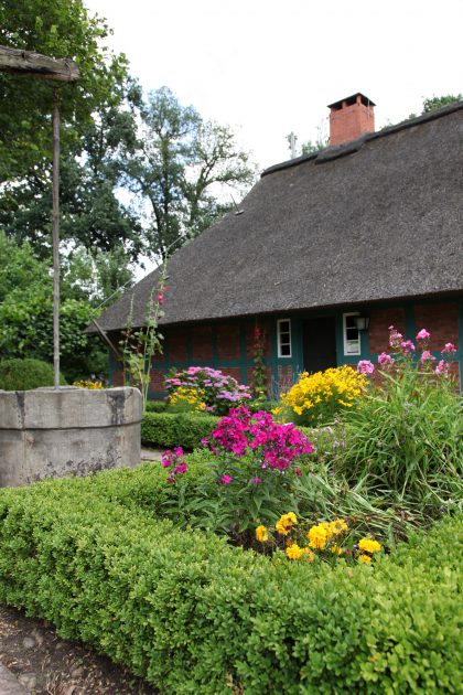 Blumen und Brunnen im Bauerngarten vor dem Bauernhaus