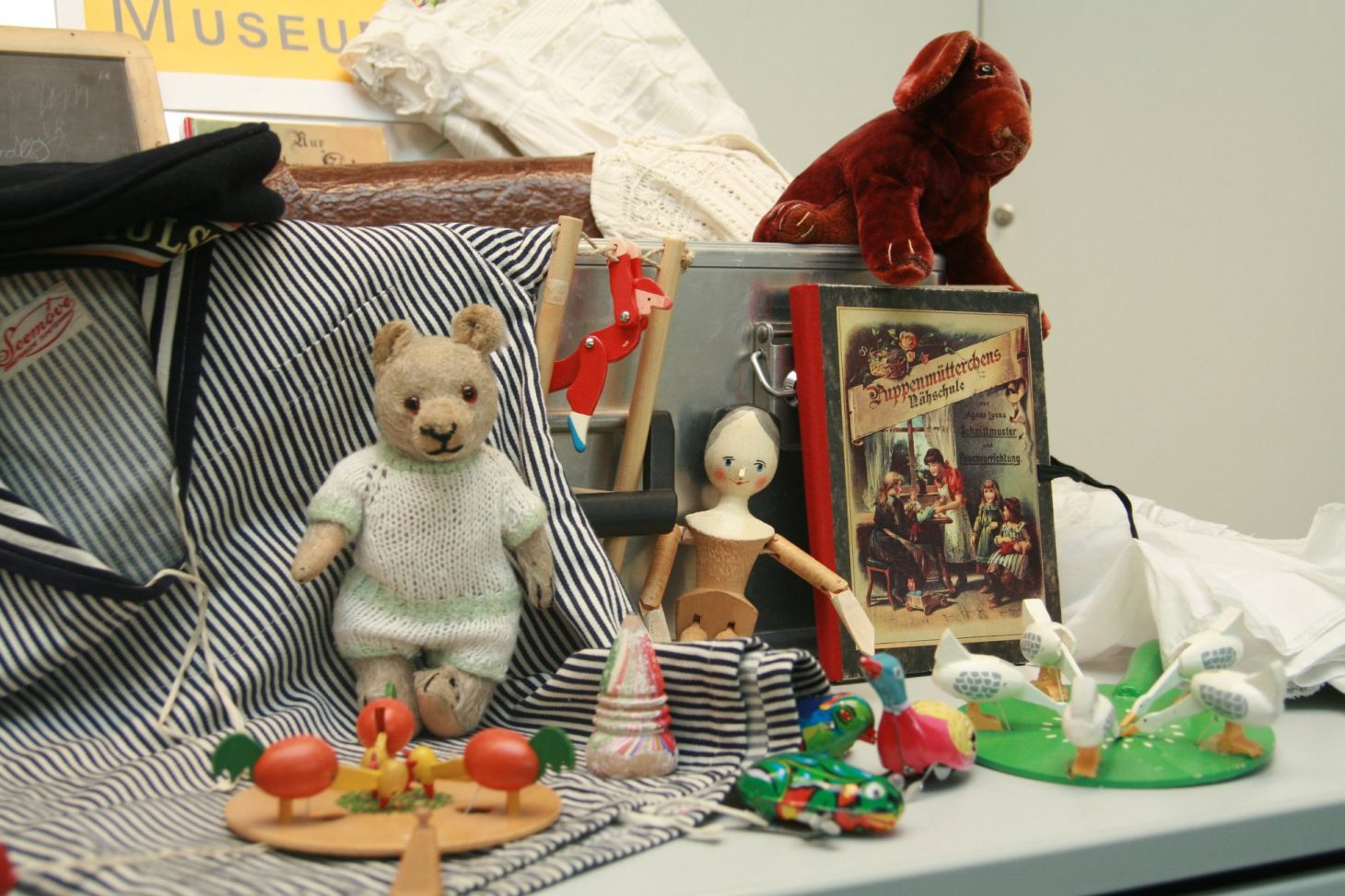 Objekte aus dem Museumskoffer: Ein Teddybär, eine hölzerne Puppe, ein Buch, ein Fischerhemd und Holzspielzeug
