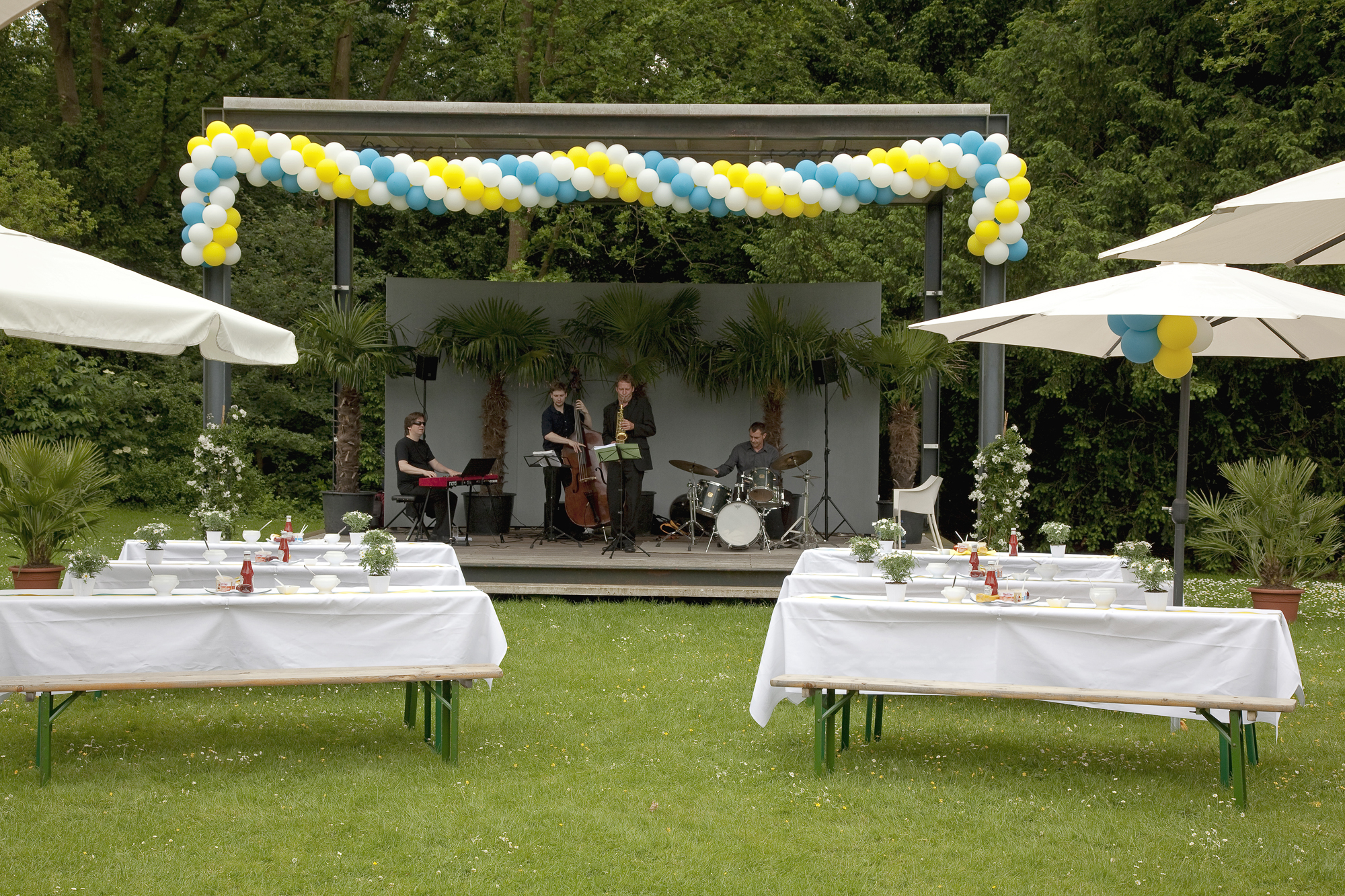 Veranstaltung im Park mit geschmückten Tischen und Band auf der Bühne. 