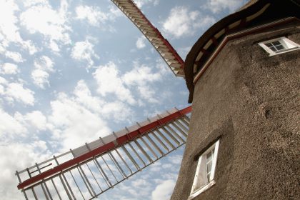 Ausschnitt der Mühle mit Flügeln vor blauem Himmel.