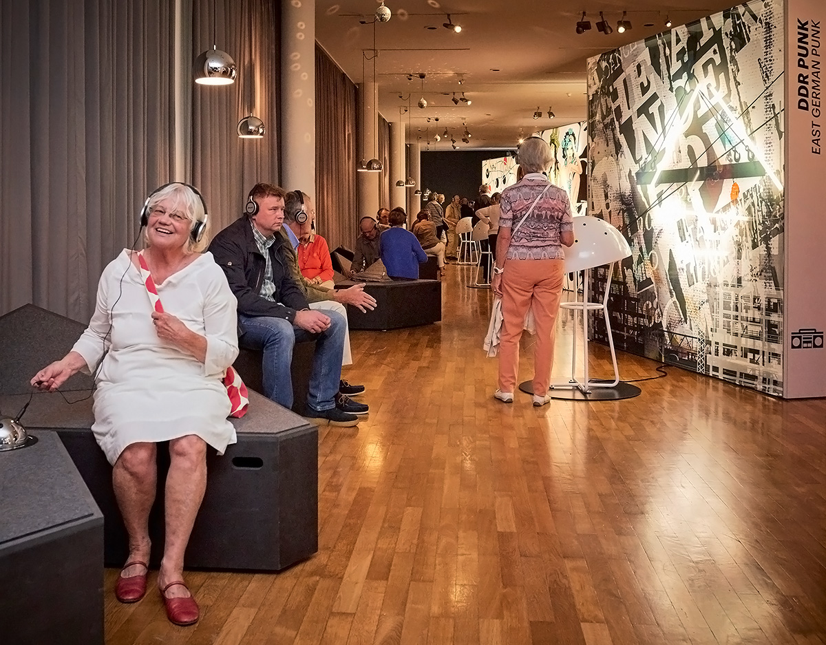 Blick in eine Sonderausstellung. Man sieht viele Besucherinnen und Besucher. Einige haben Kopfhörer auf. 