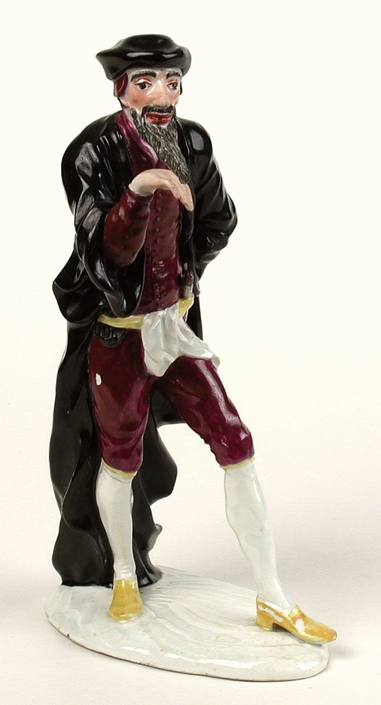 Männliche Porzellanfigur, die einen schwarzen Mantel und rote Kniebundhosen trägt. 