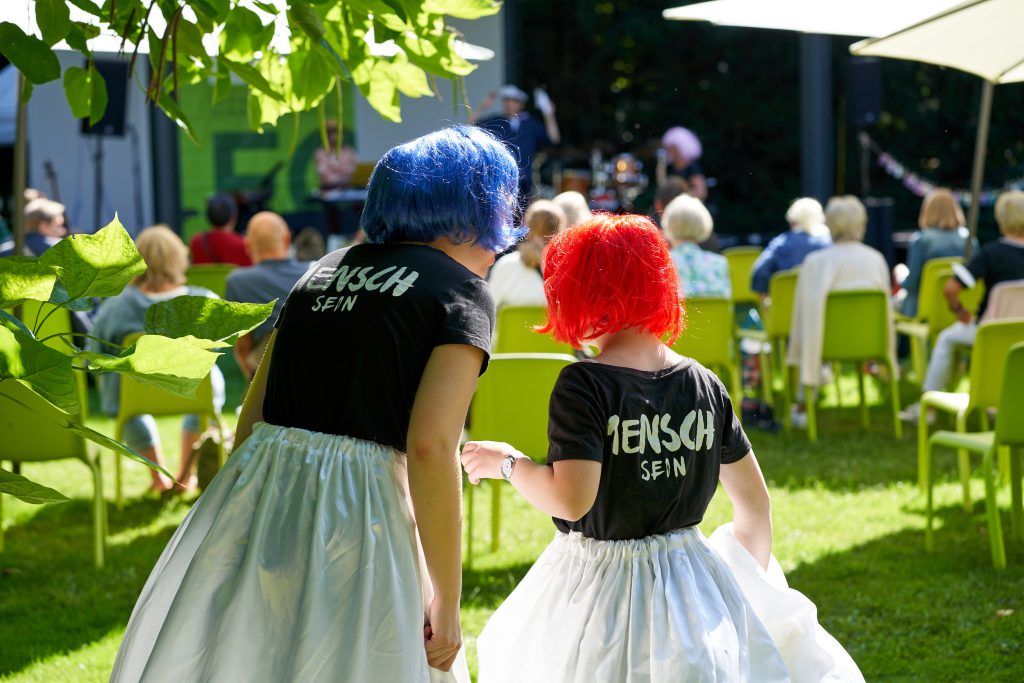 zwei Darstellerinnen des Blaumeier-Ateliers schauen auf die Bühne. Man sieht sie von hinten.