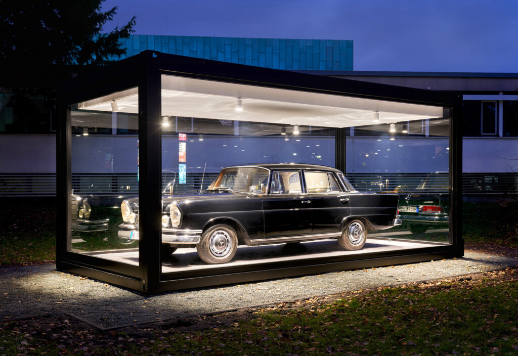 schwarzer Mercedes in beleuchteter Vitrine vor dem Museum.
