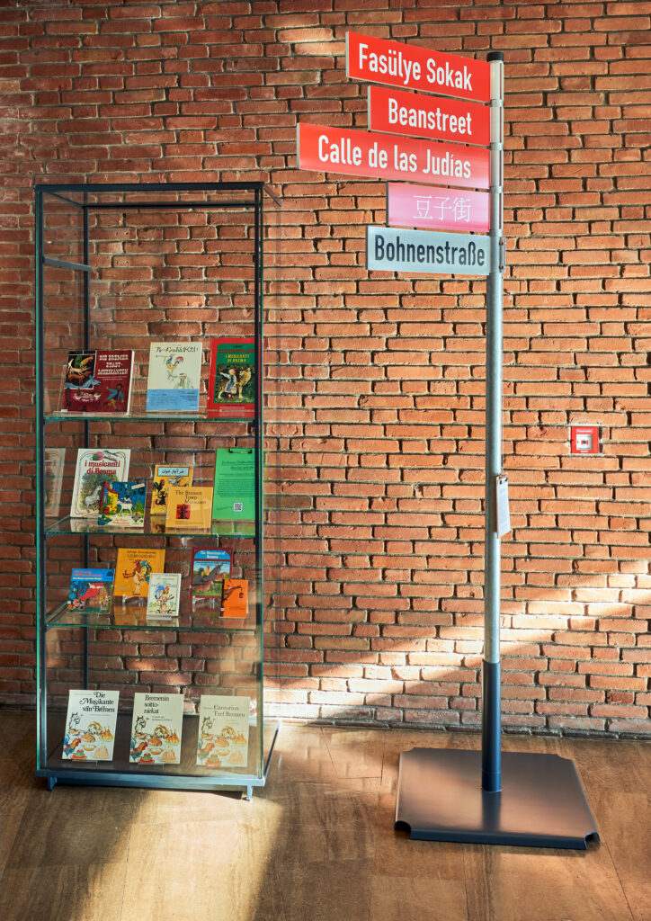 Blick in den Ausstellungsraum auf einen Wegweiser und eine Vitrine mit Büchern.