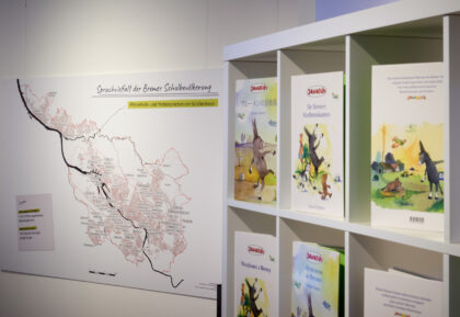 Blick auf ein Regal mit Büchern der Stadtmusikanten in verschiedenen Sprachen und eine Stadtkarte Bremens.