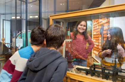 Vier Kinder schauen sich ein Objekt in einer Vitrine an.