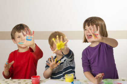 Drei Kinder halten ihre mit Farbe bemalten Hände hoch