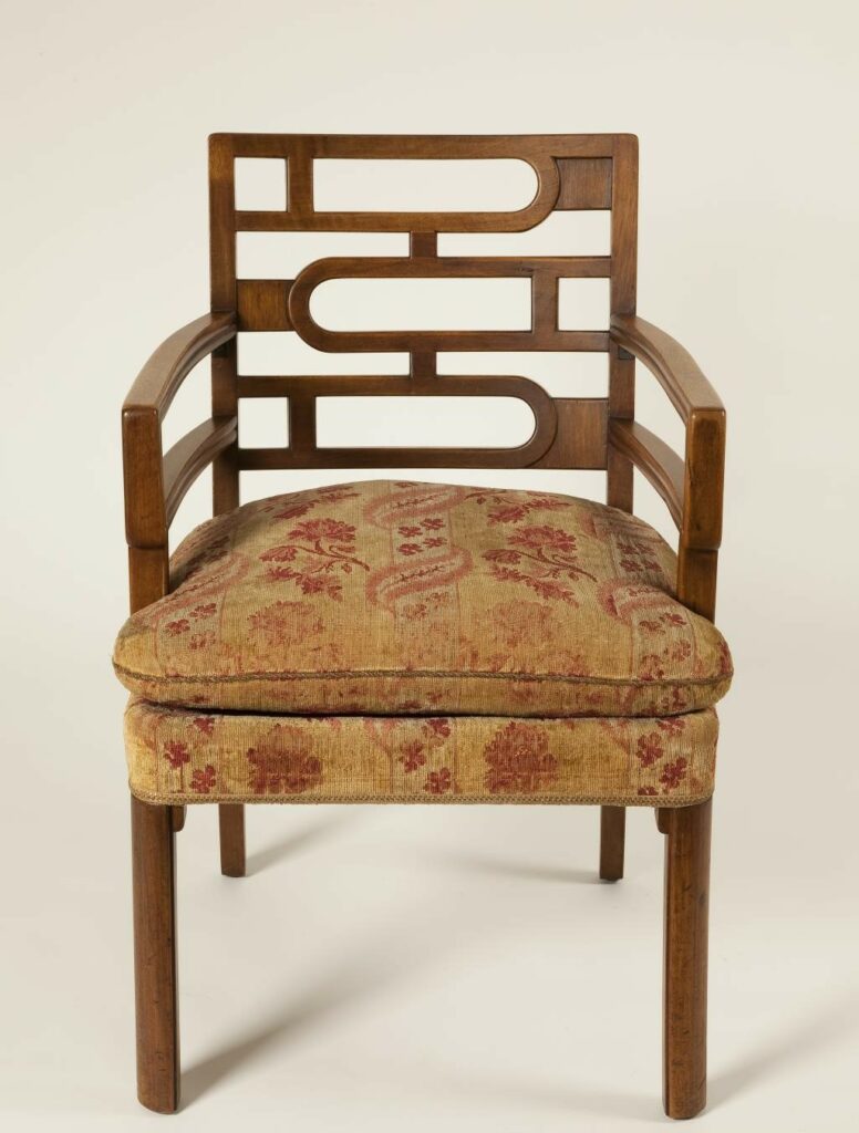 Ein Armlehnstuhl im Stil des Art déco. Der Sitz ist gepolster und mit einem Blütenstoff überzogen. 
