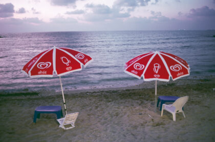 zwei kleine Tische mit Plastikstühlen unter Sonnenschirmen am Strand