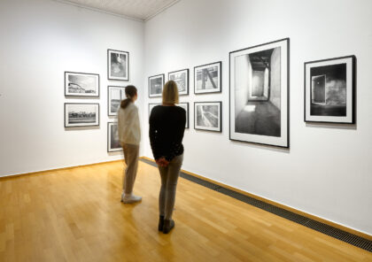 zwei Besucherinnen stehen vor einer Wand mit schwarz-weißen Fotografien.