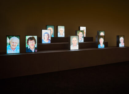 Elf beleuchtete Porträts stehen auf einem Podest.