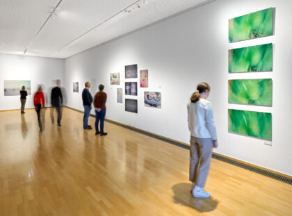Mehrere Besucherinnen und Besucher schauen sich Bilder in der Ausstellung an.