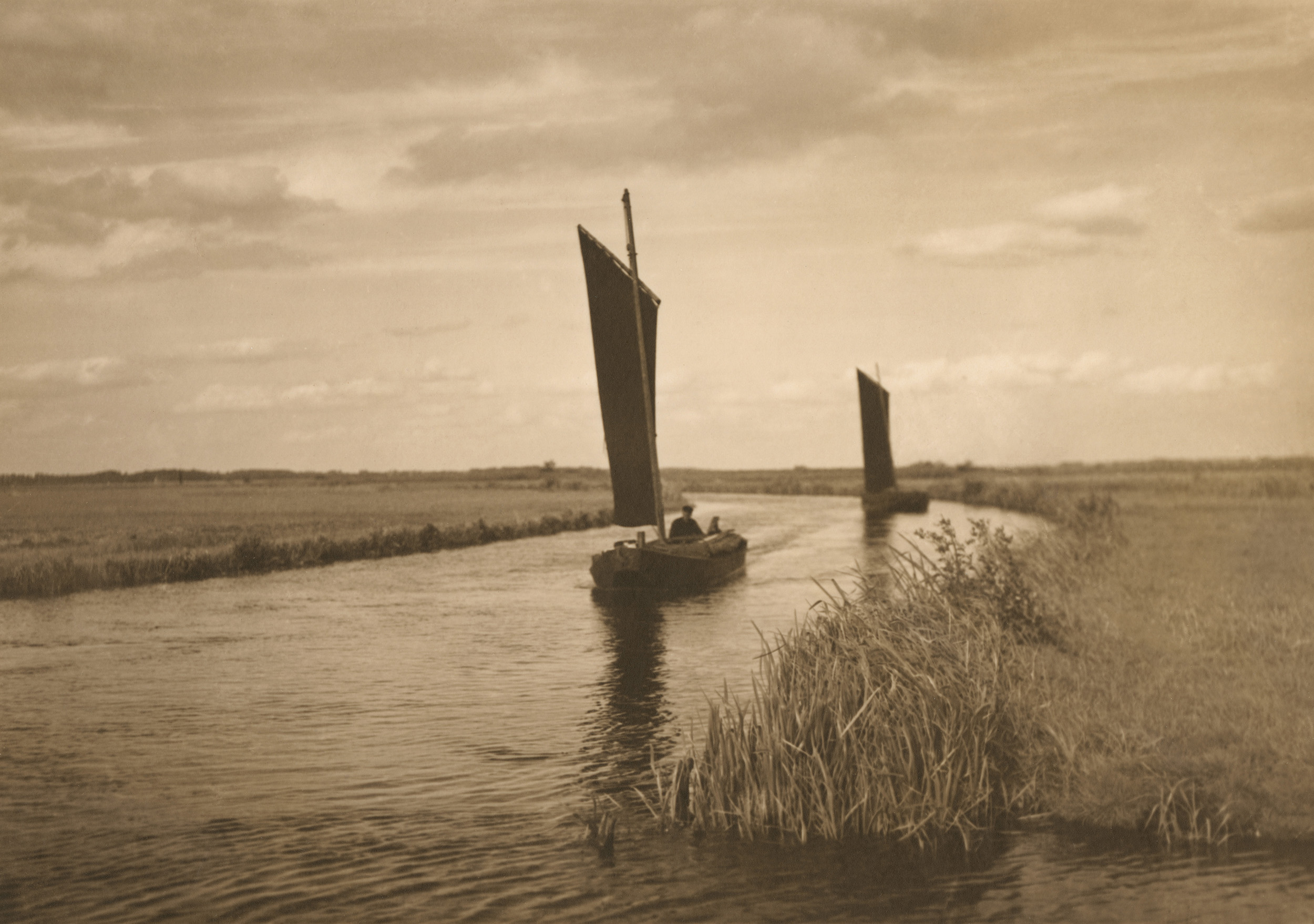 Zwei Torfkähne mit schwarzen Segeln sind auf dem Wasser unterwegs. Es handelt sich um eine Aufnahme des Ateliers Frank.     