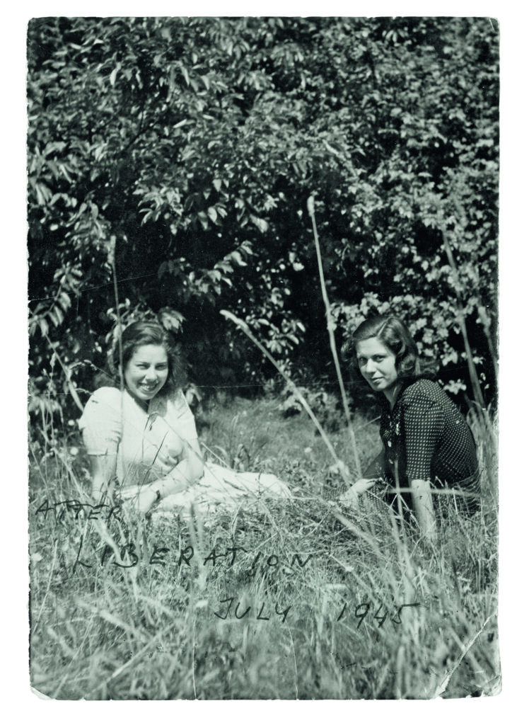 Zwei junge Frauen sitzen im Sommer auf einer Wiese. Auf dem Foto steht handschriftlich: Liberation 1945   