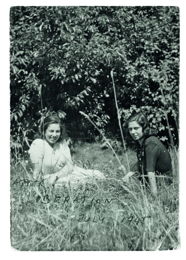 Zwei junge Frauen sitzen im Sommer auf einer Wiese. Auf dem Foto steht handschriftlich: Liberation 1945