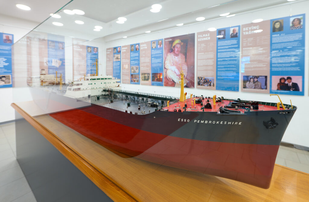 Modell eines Containerschiffs mit Bild/Texttafeln im Hintergrund.