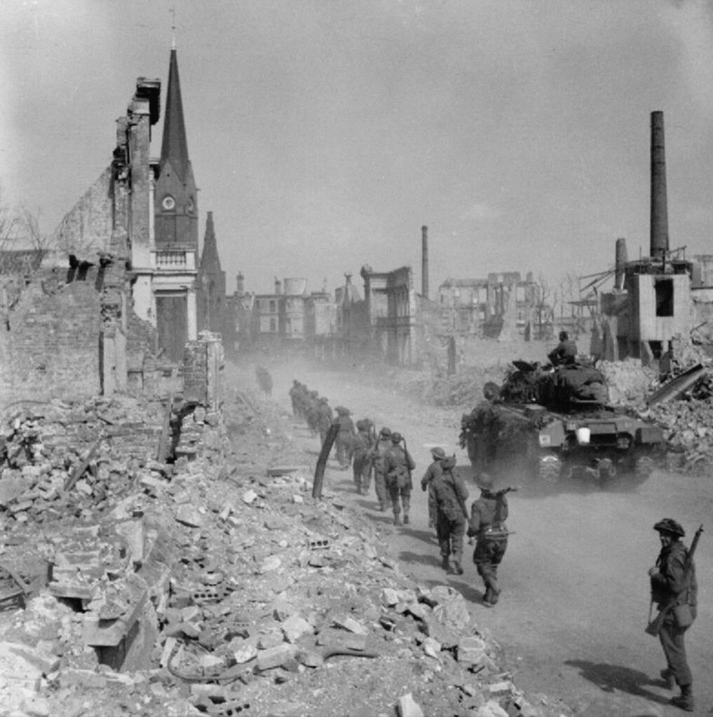 schwarz-weiß-Foto des zerstörten Bremens. Soldaten marschieren durch eine Straße. Neben ihnen fährt ein Panzer.