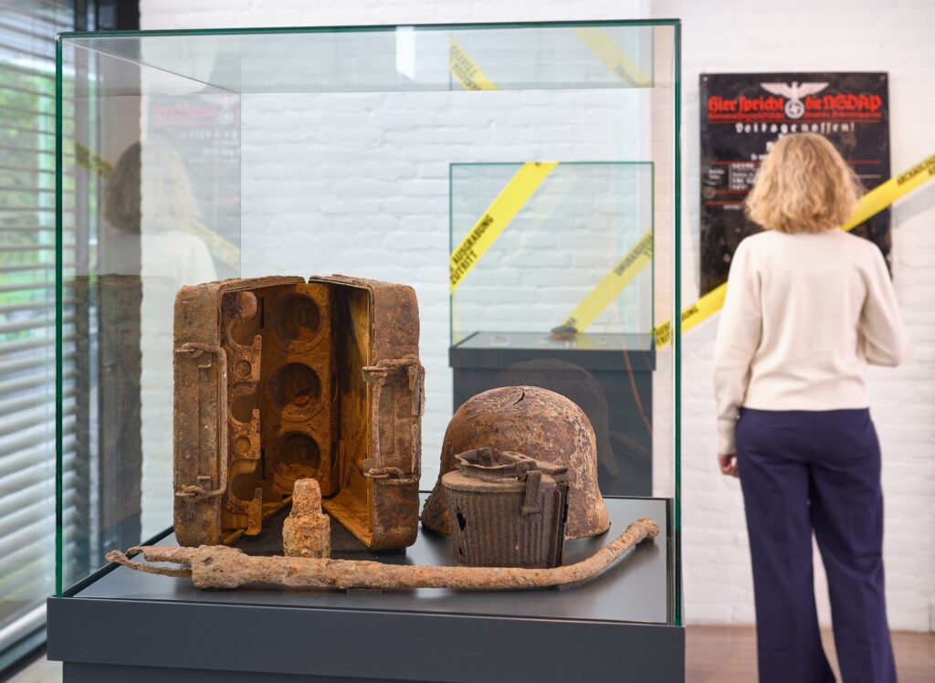 Blick in die Ausstellung. Im Vordergrund ist eine Vitrine mit verrosteten Waffen zu sehen.