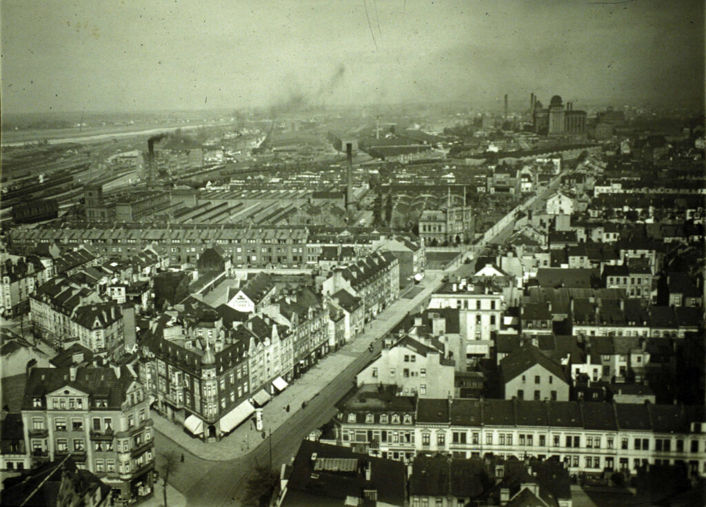 schwarz-weiß Foto eines STadtviertels aus der Vogelperspektive. Man sieht Straßenzüge, Häuser und Fabriken mit rauchenden Schornsteinen.